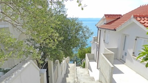 Un étroit sentier pavé de pierres mène à un bâtiment blanc surmonté d’un toit de tuiles rouges, qui surplombe une étendue d’eau.