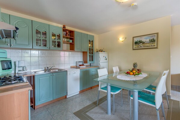 A compact kitchen with teal cabinets, a dining table with chairs, and a refrigerator.
