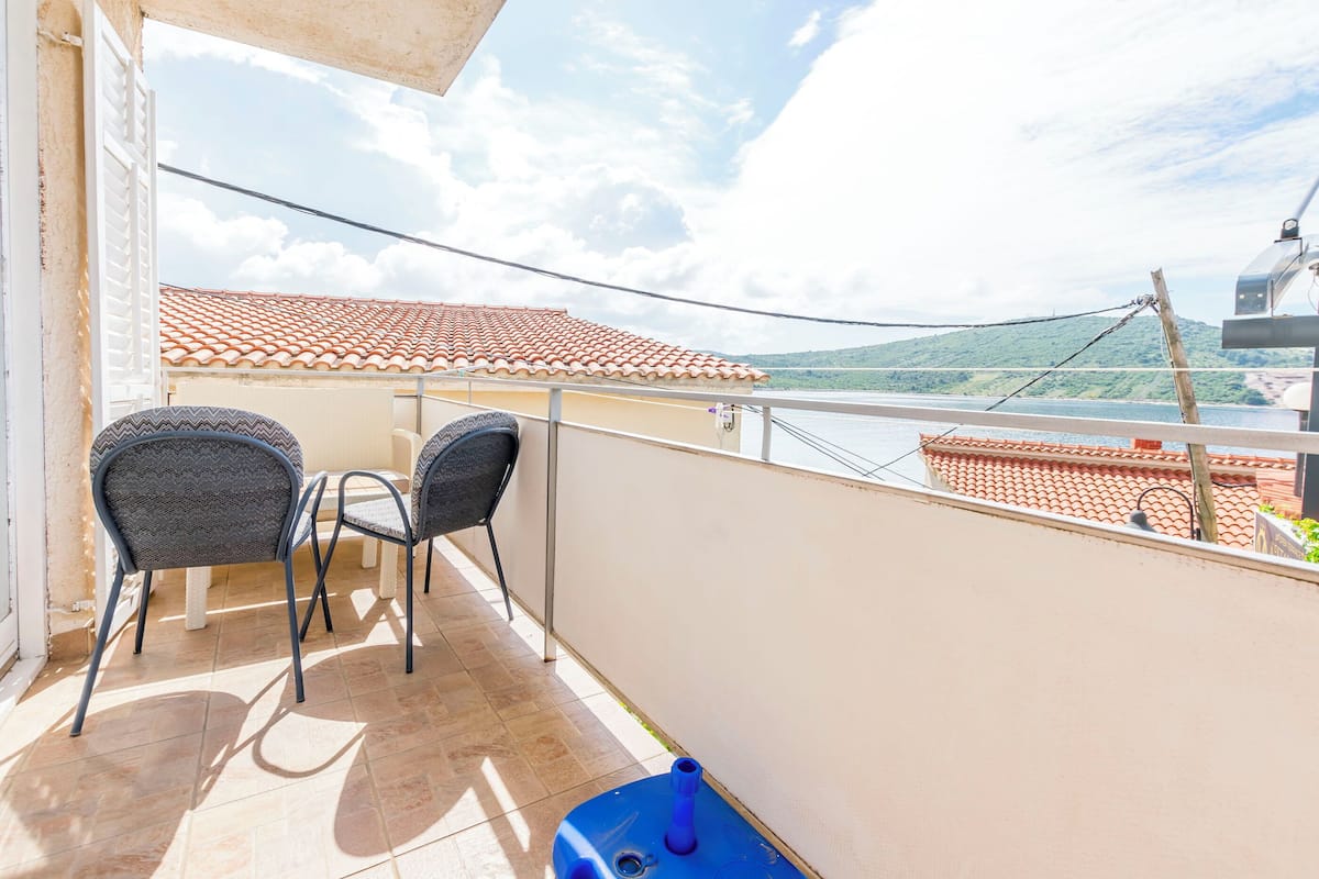 A balcony with two chairs, a table, and a blue container.