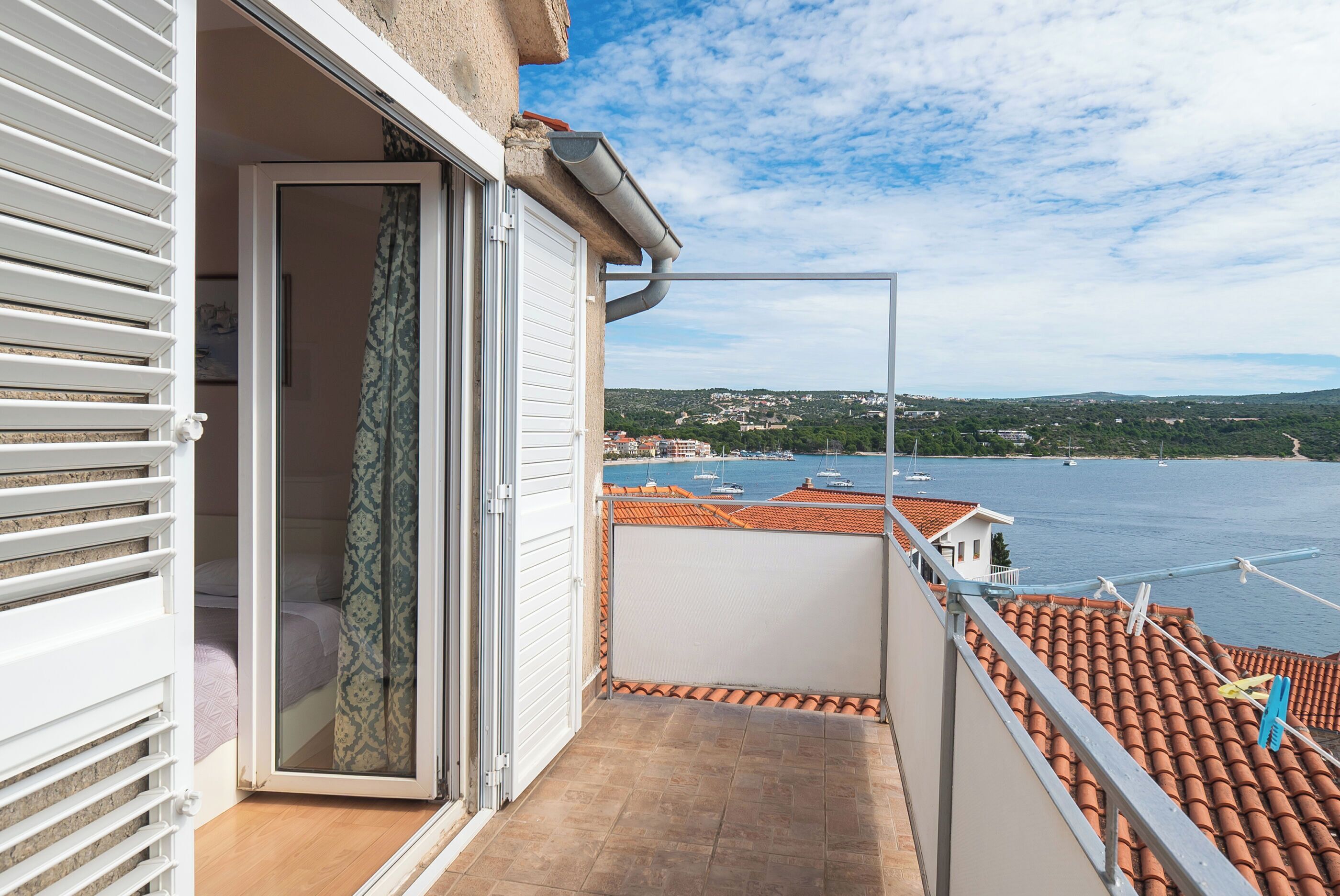 Ein Balkon mit Blick auf einen Hafen, ein Ziegeldach und eine Tür zu einem Zimmer.