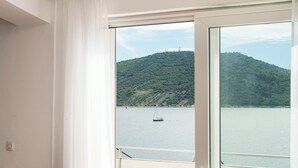 A room with a large window overlooking a body of water and a green hill. - Apartments Zivana (Primosten)