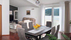 A modern living room with a dining area, a sofa set, and a large window with a view of a mountainous landscape. - Apartments Zivana (Primosten)