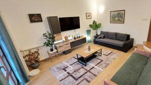 Una sala moderna con una televisión de pantalla plana, un sofá gris, una mesa de centro de madera y una alfombra estampada.