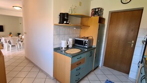 Cocina pequeña con microondas, cafetera y un armario de madera.
