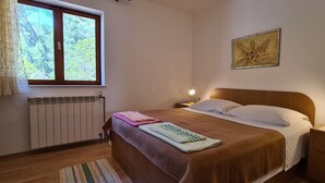 Un dormitorio con cama de madera, un radiador, una ventana con cortinas, una lámpara de noche y una obra de arte colgada en la pared.