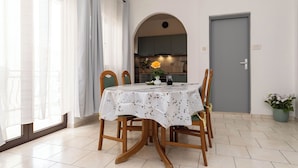 Een eetgedeelte met een tafel voor vier personen, een keuken op de achtergrond en een grijze deur.