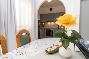 A dining table with a lace tablecloth, a vase with a yellow flower, and a bowl of snacks. - Apartments Tonja (Primosten)