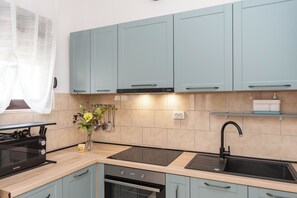 A modern kitchen with light blue cabinets, a black stove, and a sink. - Apartments Tonja (Primosten)