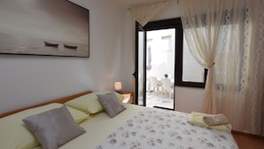 Een slaapkamer met een bed, kussens, een dekbed, een raam met gordijnen en uitzicht op het omliggende landschap.