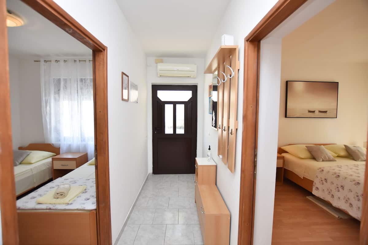 A narrow hallway leading to a bedroom with a bed, a bedside table, and a wooden bench.