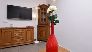 Un salon moderne avec un téléviseur à écran plat, des meubles en bois, un vase rouge orné de fleurs et un lampadaire.