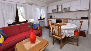 Un espace de vie compact comprenant un canapé rouge, une table à manger avec des chaises, un coin cuisine avec des meubles blancs et une fenêtre agrémentée de rideaux légers.