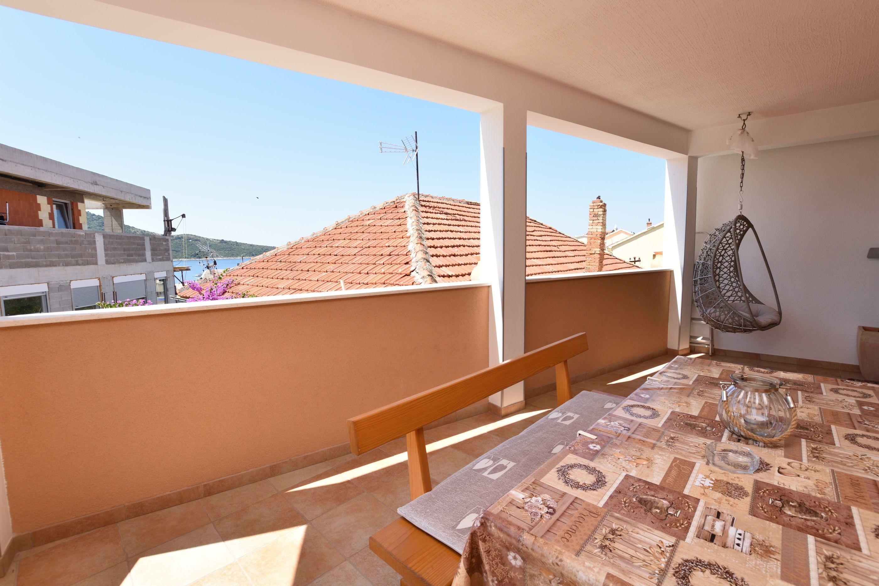 Un balcón con mesa, banco, silla colgante y vistas a edificios y colinas.
