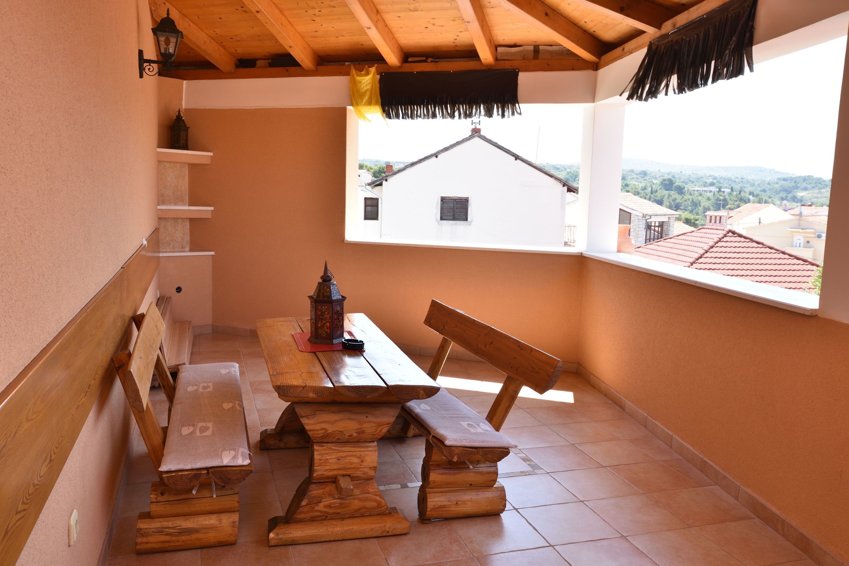 A wooden bench and table set up in a corner with a view of a white building and hills in the background.