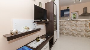 A modern kitchen with a flat-screen TV mounted on a wooden shelf, a decorative doily, and a small table with a laptop. - Apartments Caric (Ivan Dolac)