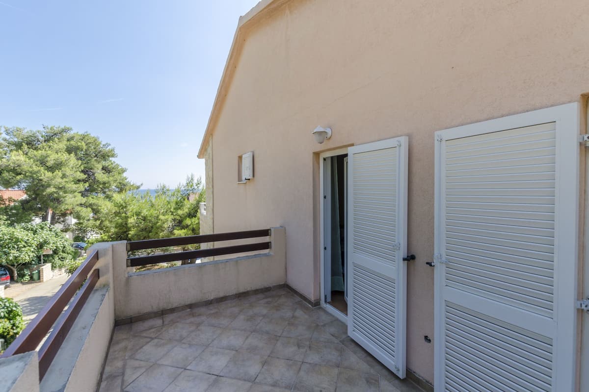 Un balcon avec un sol carrelé, une balustrade et deux volets blancs.