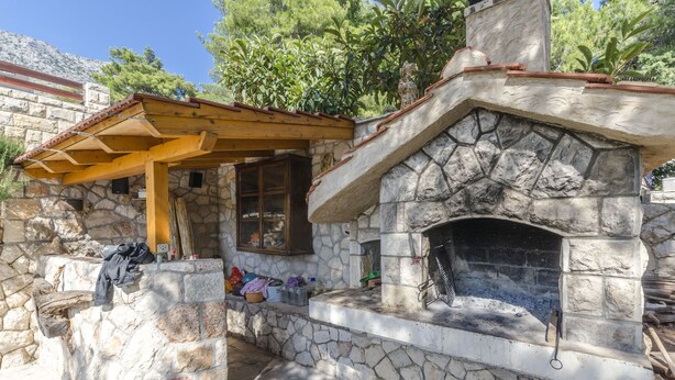 A stone-built outdoor kitchen with a built-in grill and a wooden pergola. - Apartments Caric (Ivan Dolac)