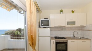 A compact kitchen with a gas stove, oven, and a small TV on top of a white refrigerator. - Apartments Caric (Ivan Dolac)