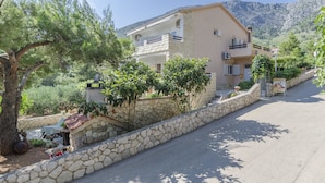 A two-story building with a stone facade, a balcony, and a stone wall along the street. - Apartments Caric (Ivan Dolac)