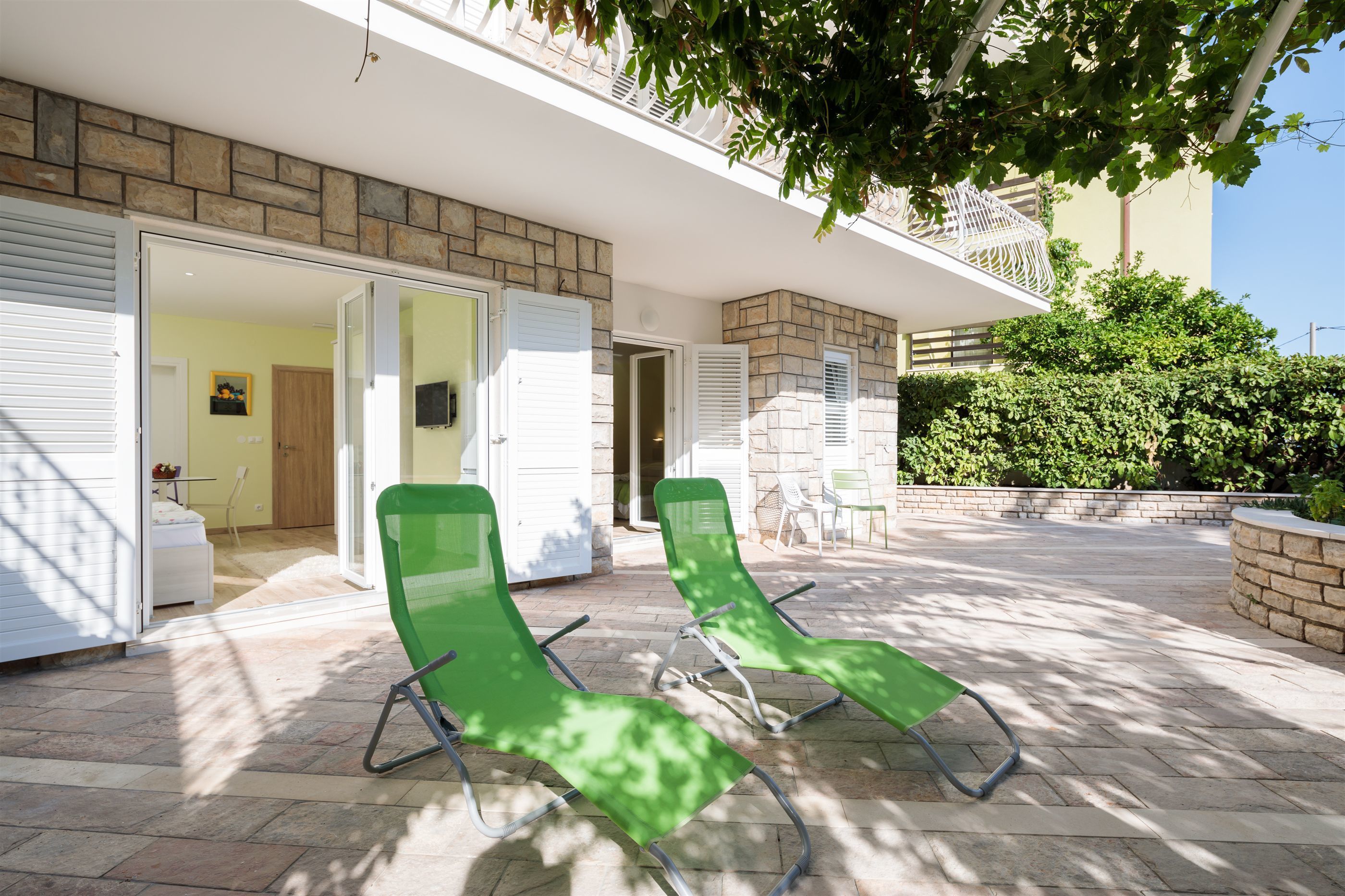 A modern outdoor area with two green lounge chairs, a stone wall, and a door leading to an interior space.