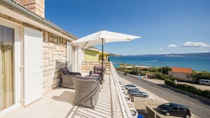 A balcony with wicker furniture, a white umbrella, and a view of the sea and distant landscape. - Apartments and Room Alen (Duce)