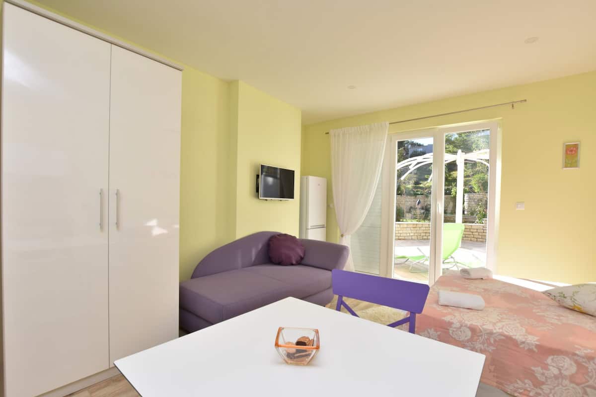 A room with a white table, purple sofa, and a bed with a floral bedspread.