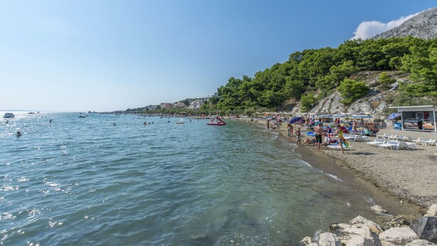 A beach with clear water, umbrellas, and people. - Apartments and Room Alen (Duce)