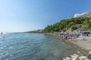 A beach with clear water, umbrellas, and people. - Apartments and Room Alen (Duce)