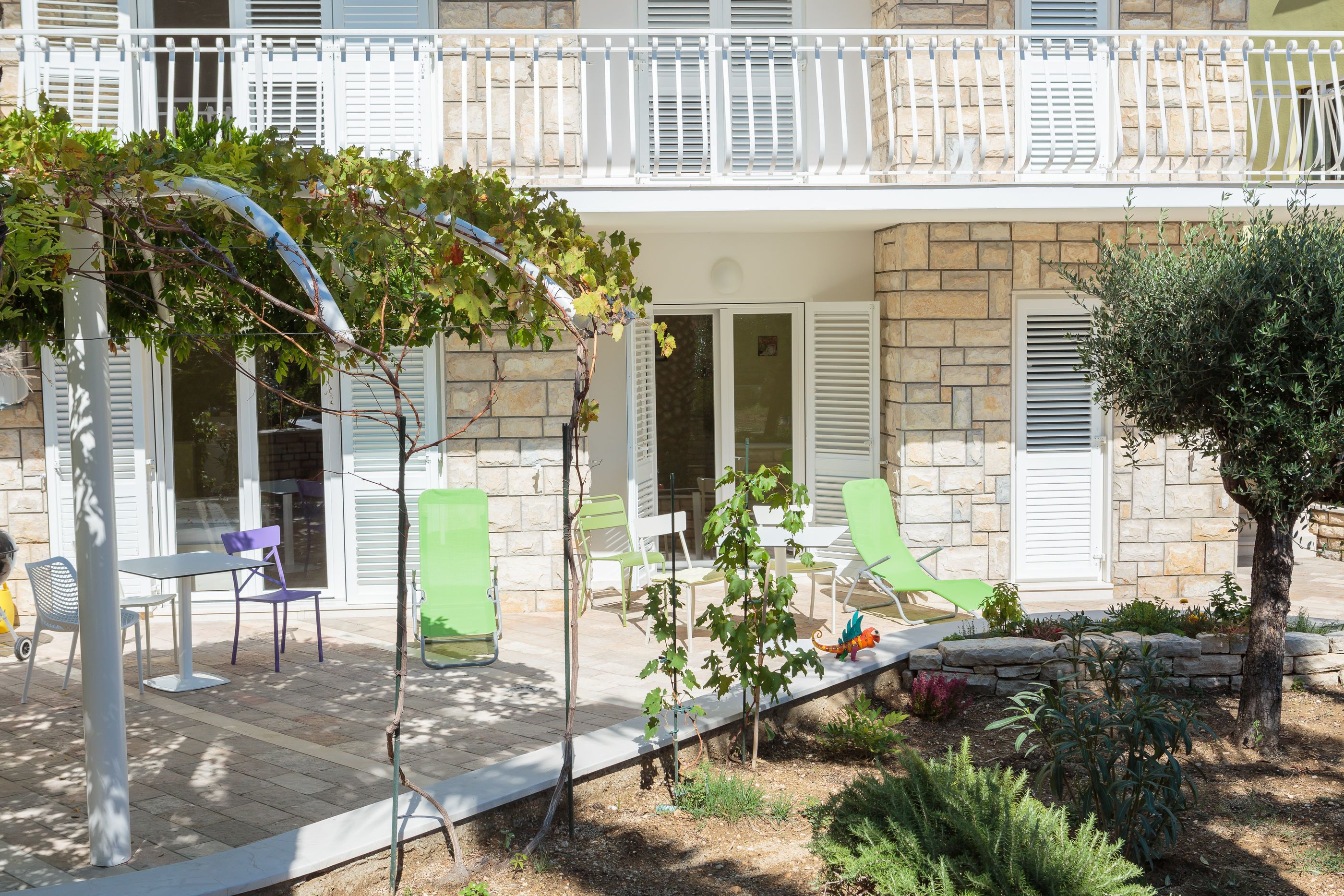 A stone building with a balcony, outdoor seating, and a garden area.