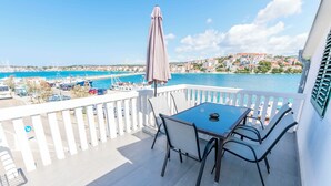 A balcony with a table and chairs, overlooking a marina and coastal town. - Apartments Olivera (Rogoznica)