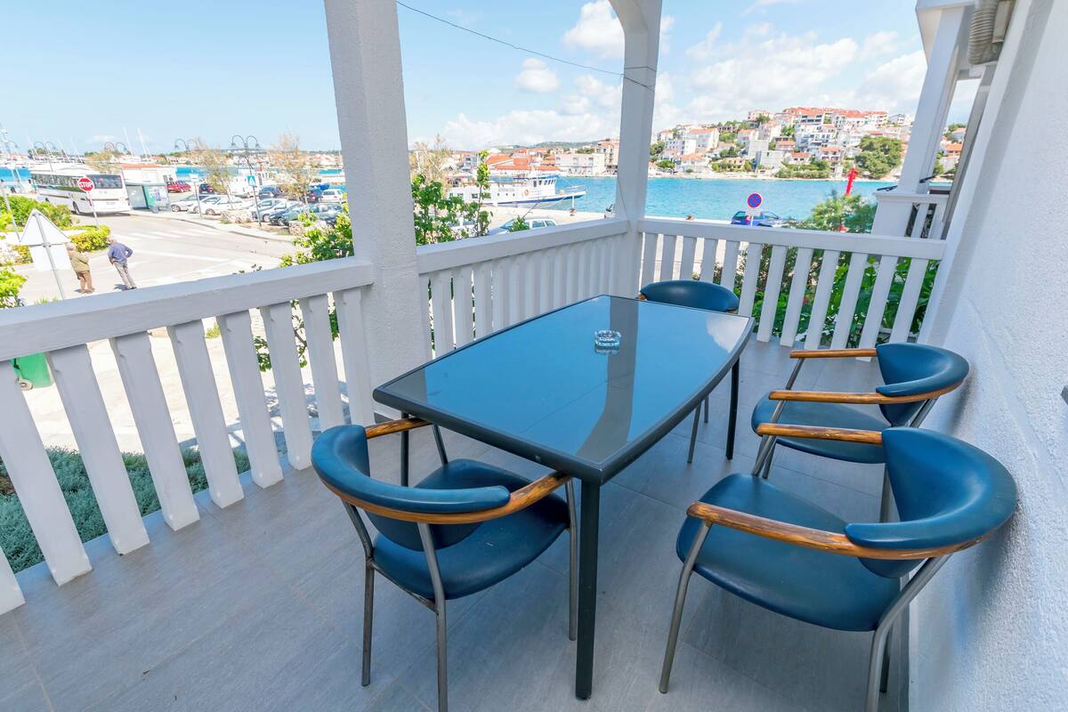 Un balcon doté d’une table en verre et de quatre chaises, offrant une vue sur une marina et une ville côtière.