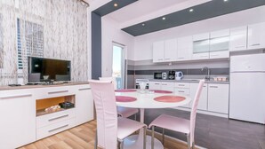 A modern kitchen with white cabinets, a dining table with pink chairs, and a flat-screen TV on a stand. - Apartments Olivera (Rogoznica)