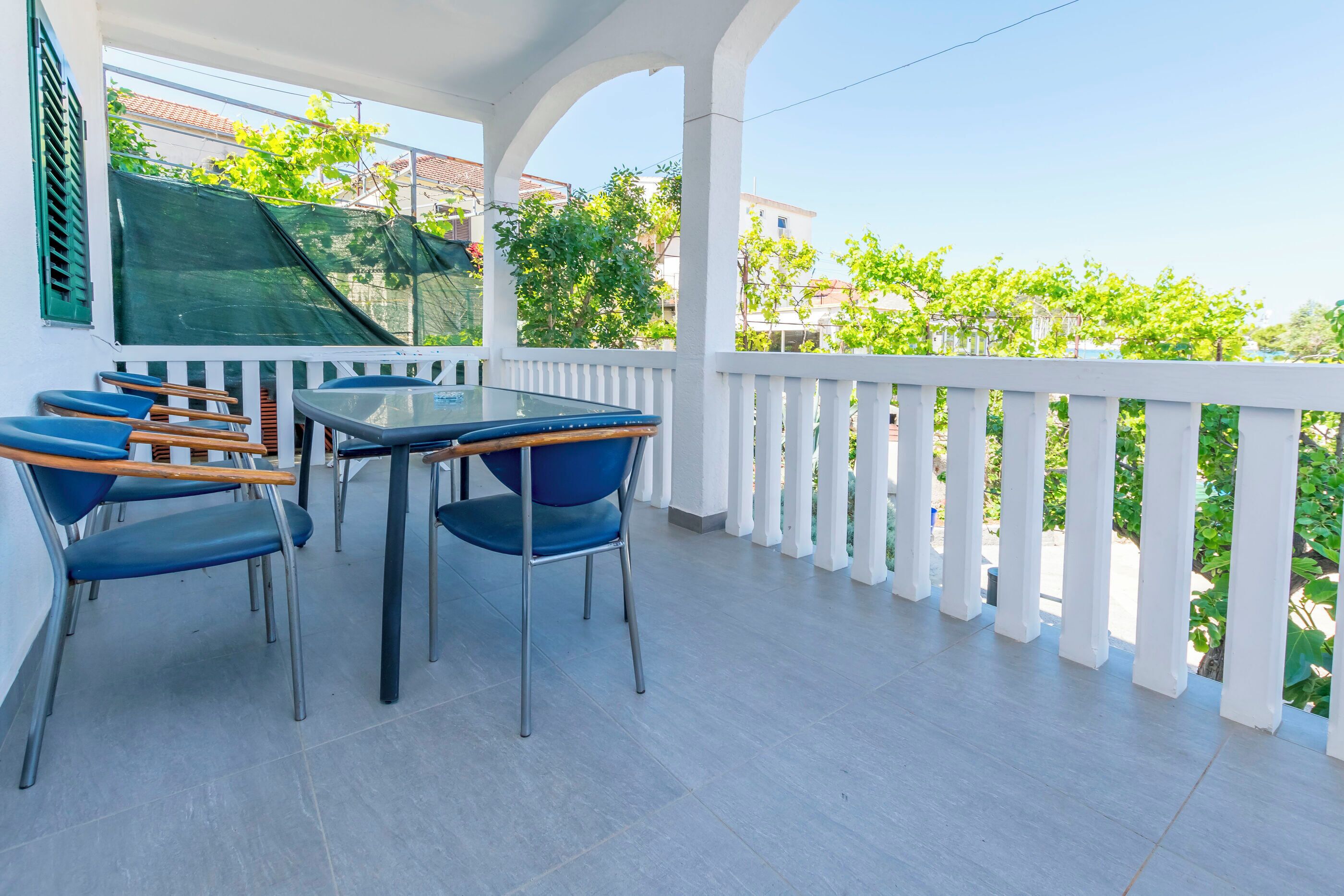 Ein Balkon mit Tisch und Stühlen, einem weißen Geländer und Blick auf Grünflächen und Gebäude.