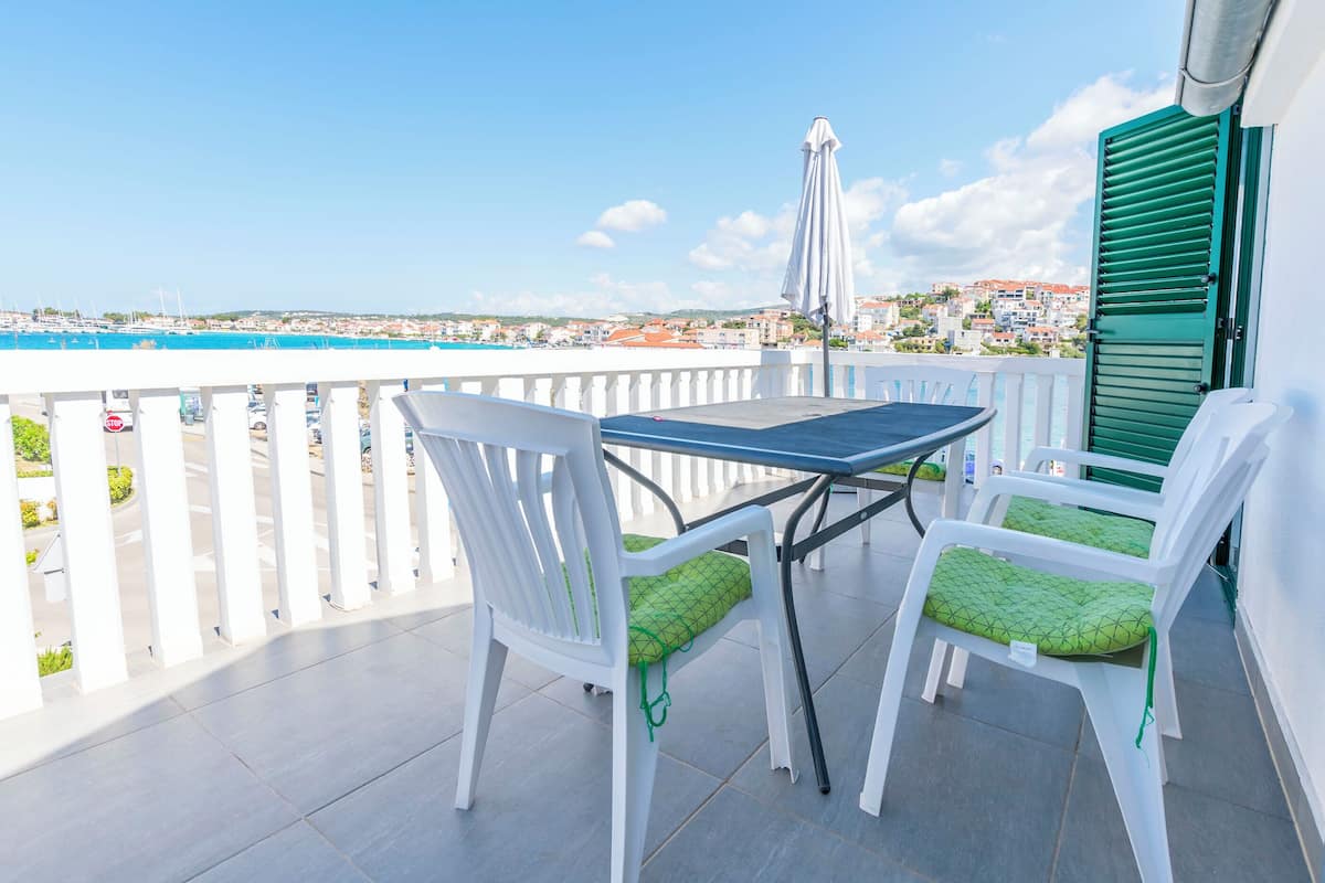 Un balcon avec une table et deux chaises, offrant une vue sur la côte, avec des bâtiments et un pont.