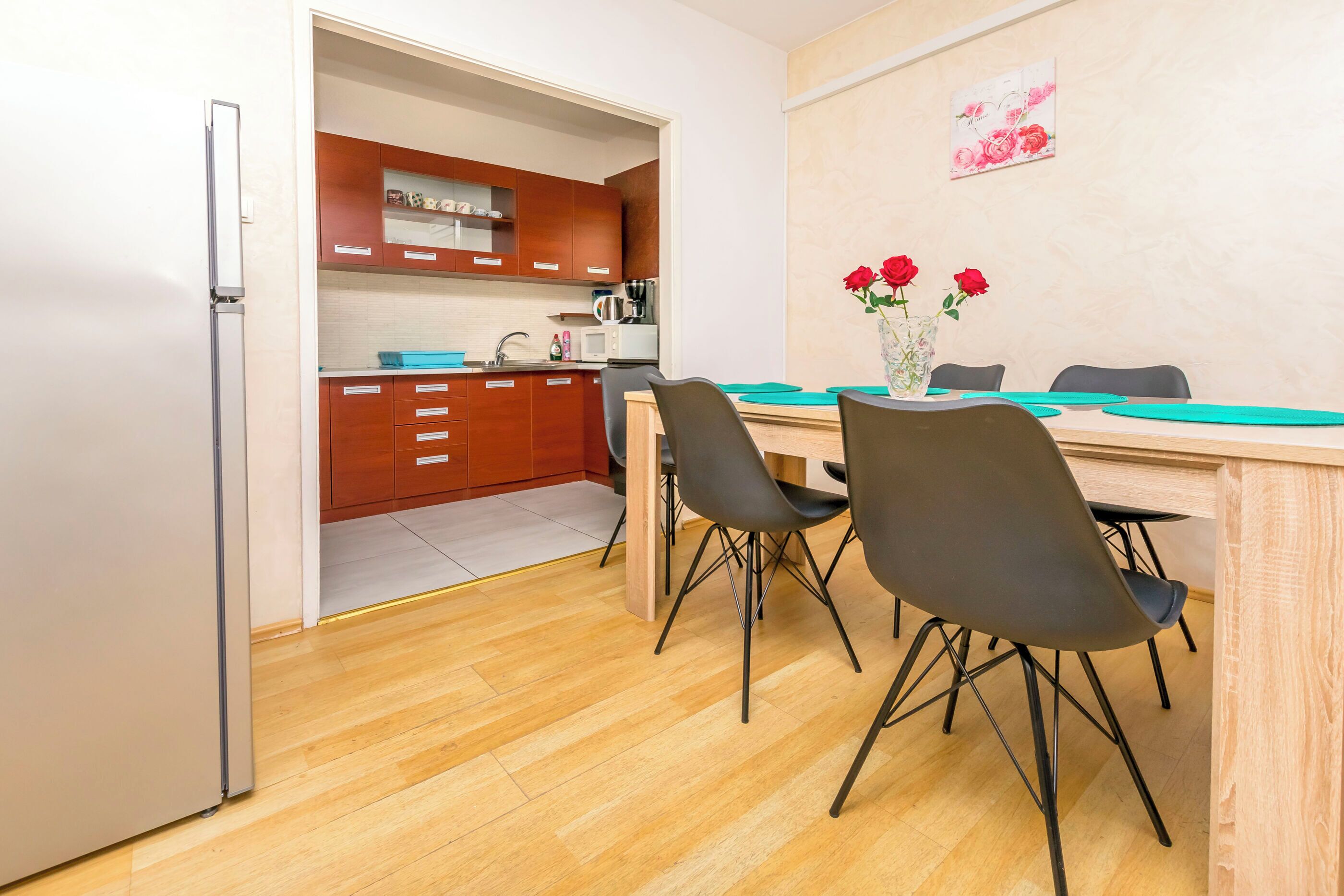 A compact kitchen with wooden cabinets, a refrigerator, and a dining area with a table and chairs.
