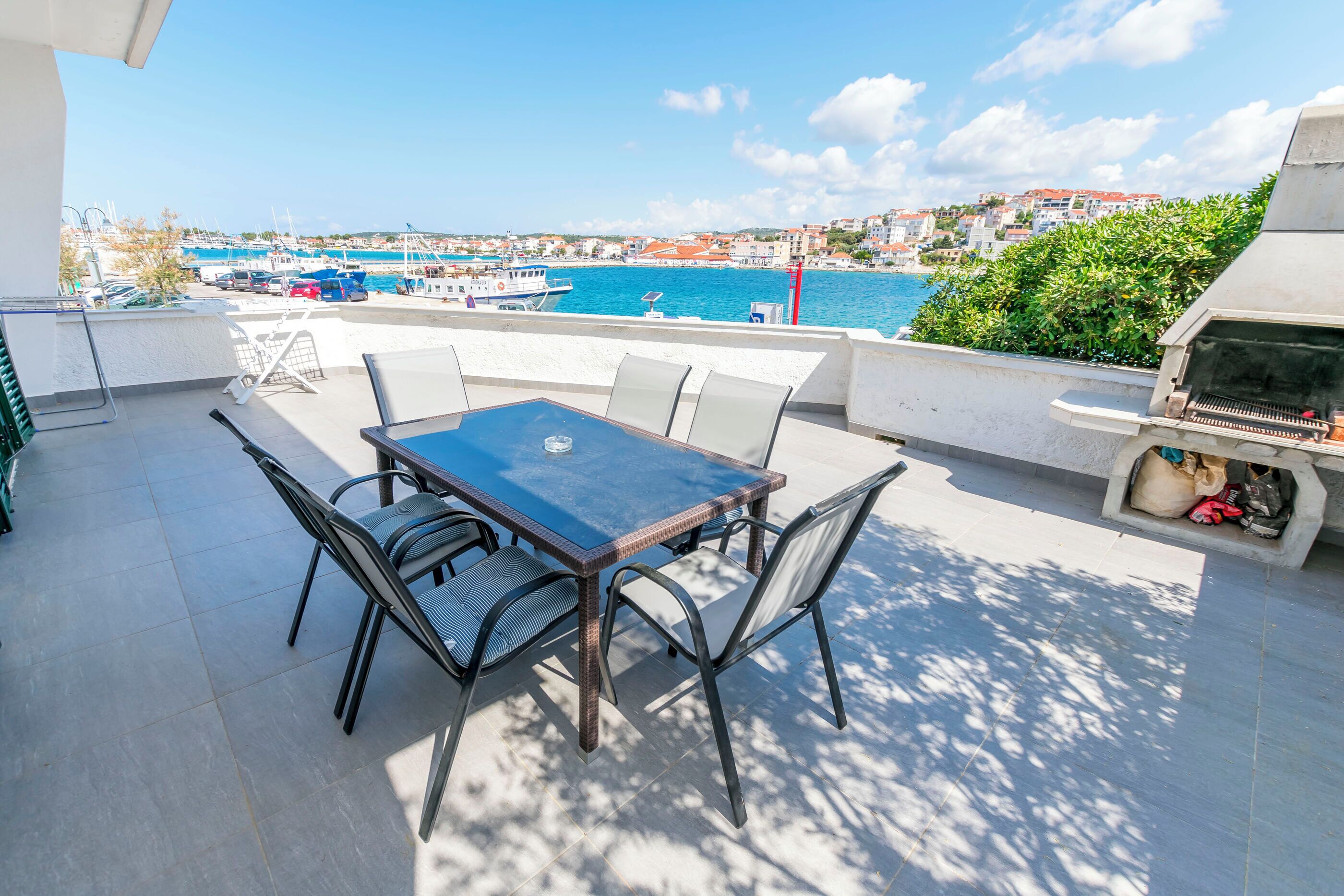 Terraço com mesa e cadeiras, com vista para uma marina com barcos e uma cidade costeira.
