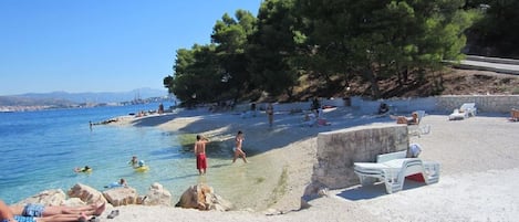 A beach with clear blue water, people swimming and sunbathing, and a rocky outcrop with a small white structure.