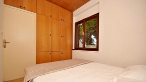 A bedroom with a bed, wooden wardrobe, and a window with a view of trees. - Apartment Jakov (Okrug Donji)