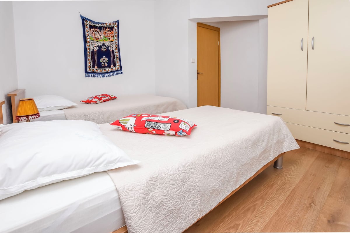 A bedroom with two beds, a wardrobe, a tapestry, and a lamp.