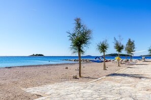 A beach with a stone pathway, trees, and a clear blue sky. - Apartments Suncica (Rogoznica)