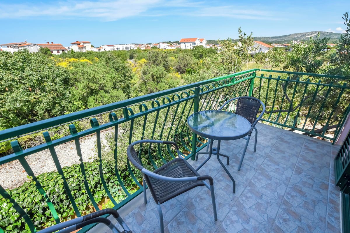 A balcony with a green metal railing, two wicker chairs, and a small round table.