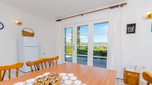 Zona pranzo con tavolo in legno, sedie, frigorifero bianco e vista sul verde circostante.
