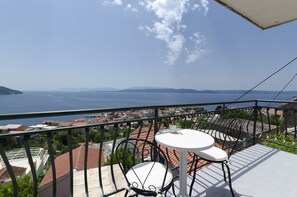 Ein Balkon mit Tisch und Stühlen mit Blick auf eine Küstenstadt und das Meer.