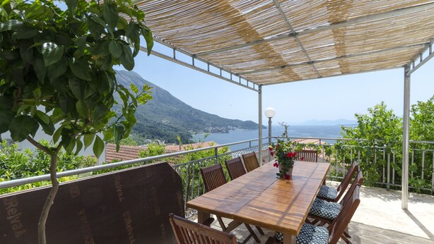 An outdoor dining area with a wooden table and chairs, a pergola, and a view of a mountainous landscape and sea. - House Jasna (Igrane)
