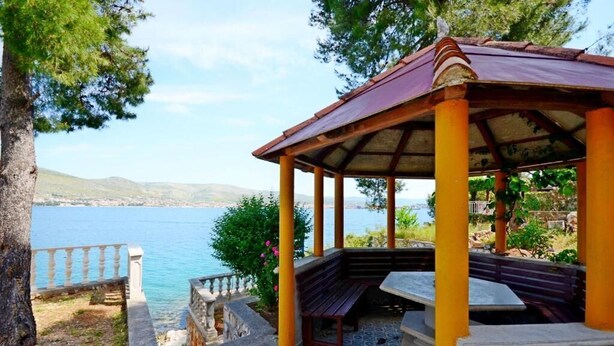 Un belvédère avec un banc donnant sur une étendue d’eau, entouré d’arbres et d’une balustrade en pierre.