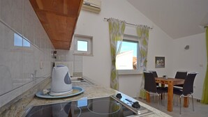 A kitchen with a stove, a kettle, and a dining table with chairs. There is a window with curtains and a small window above the stove. - Apartments Mara (Vodice)