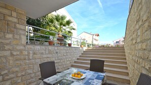 A stone-walled outdoor seating area with a table set for two, featuring a plate of oranges. - Apartments Mara (Vodice)