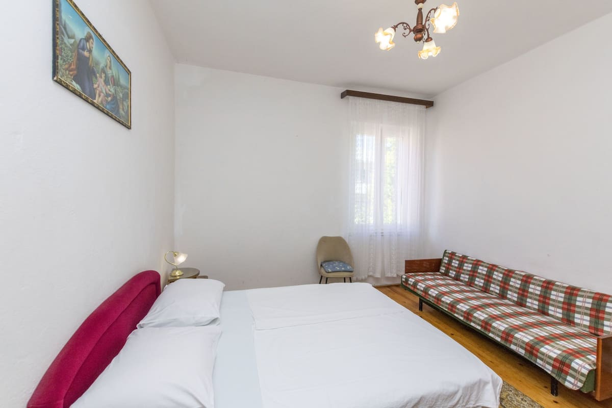 Un dormitorio con cama, sillón, sofá, un cuadro en la pared y una ventana con cortinas.