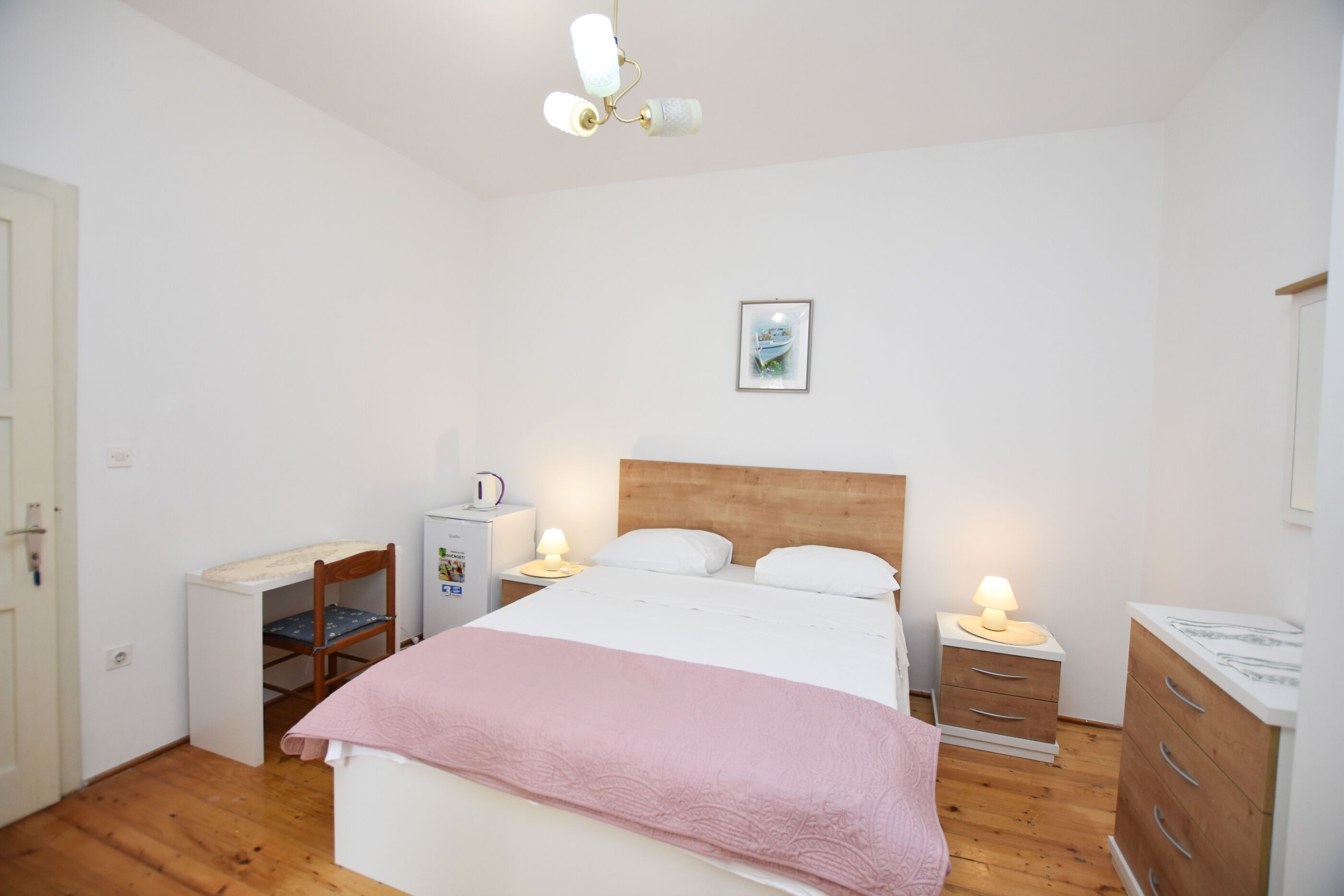 A bedroom with a bed, bedside tables, a dresser, a chair, a desk, and a ceiling light fixture.