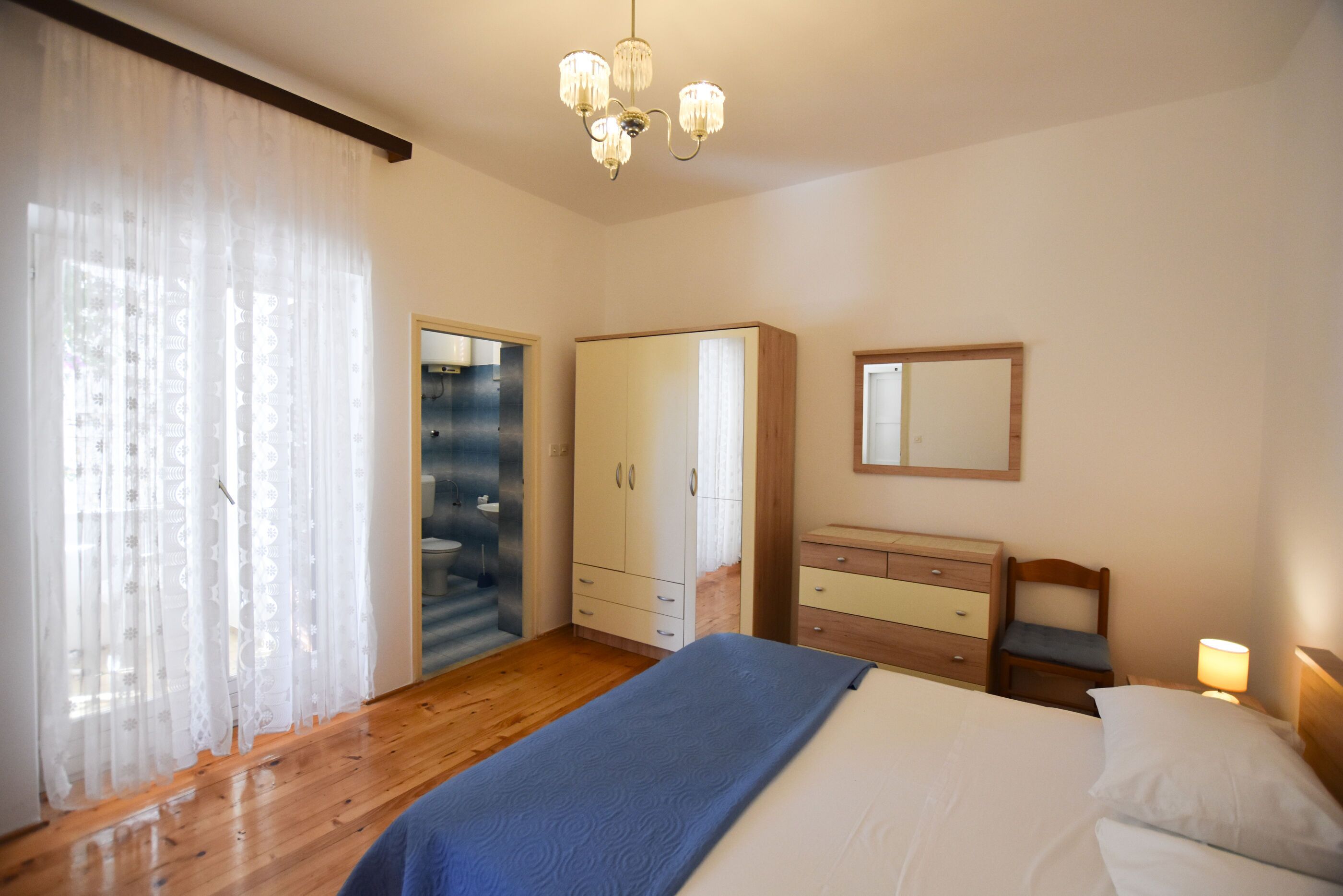 A bedroom with a bed, a wardrobe, a dresser, a mirror, and a chandelier.